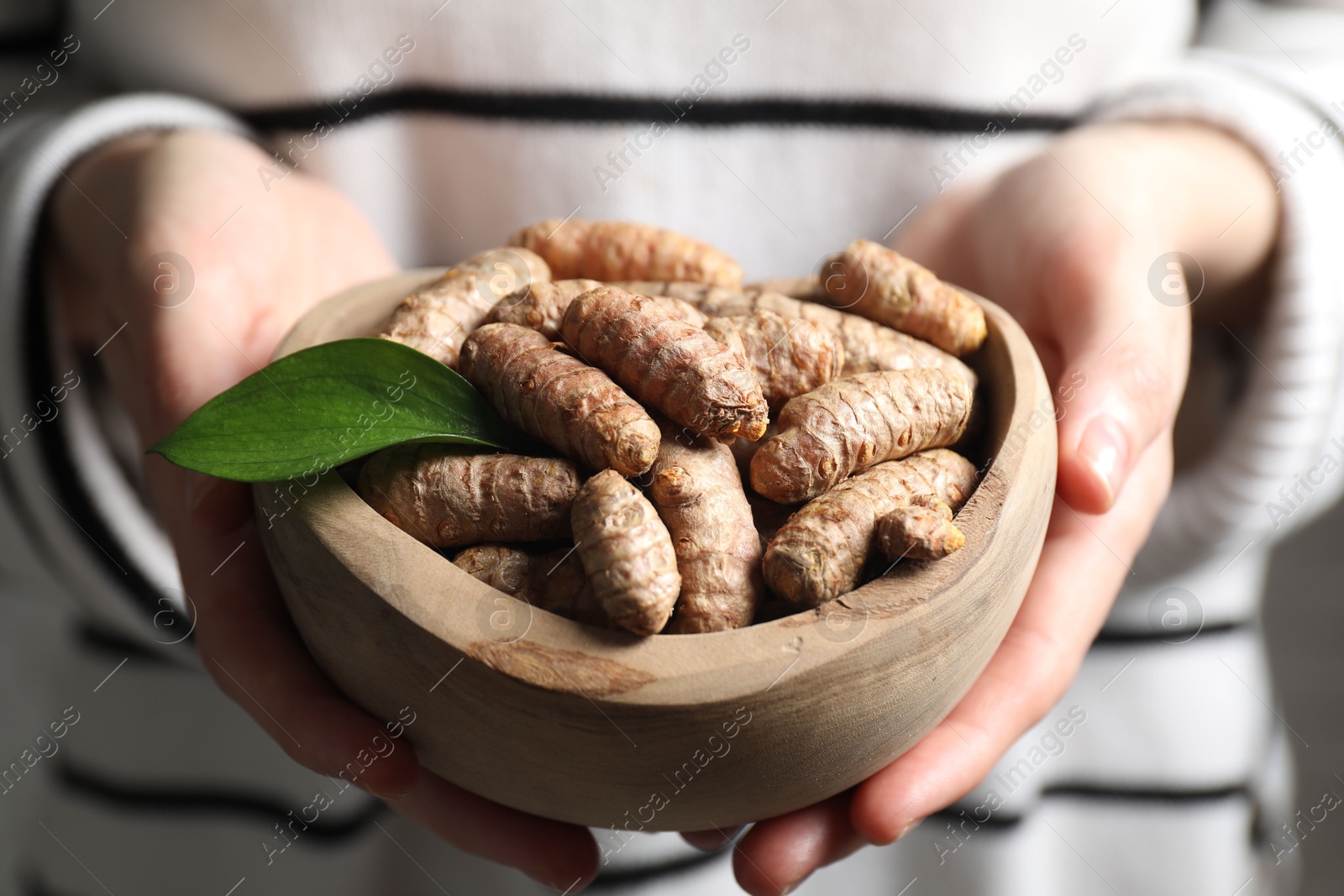 Photo of Woman holding bowl with raw turmeric roots, closeup