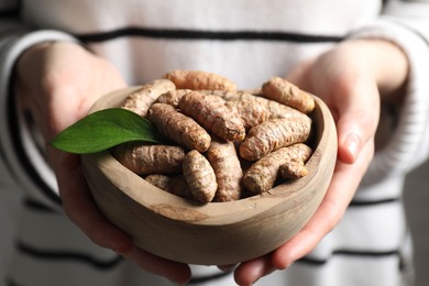 Photo of Woman holding bowl with raw turmeric roots, closeup