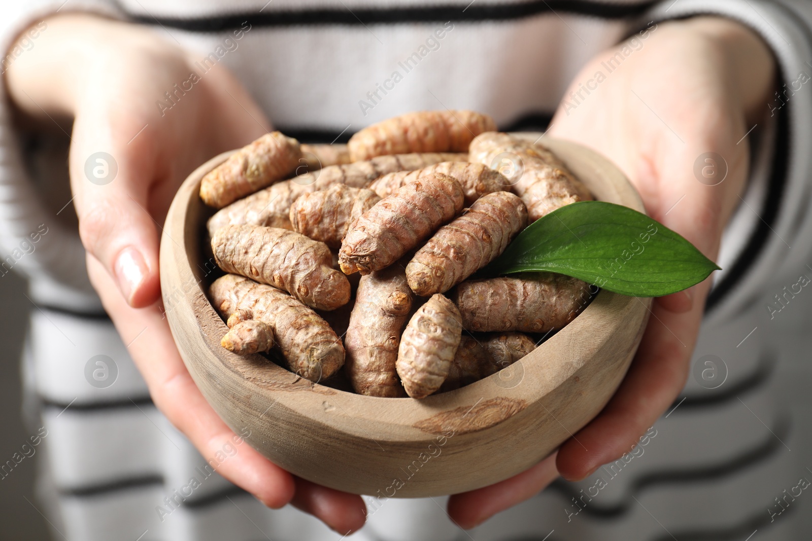 Photo of Woman holding bowl with raw turmeric roots, closeup