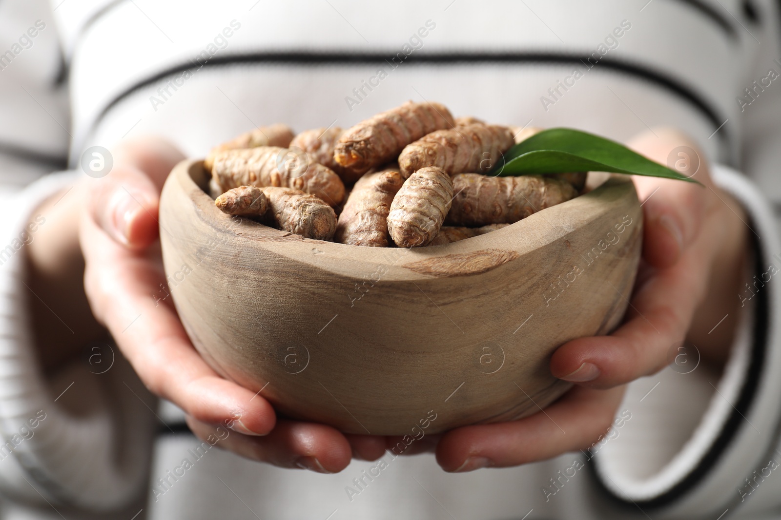 Photo of Woman holding bowl with raw turmeric roots, closeup