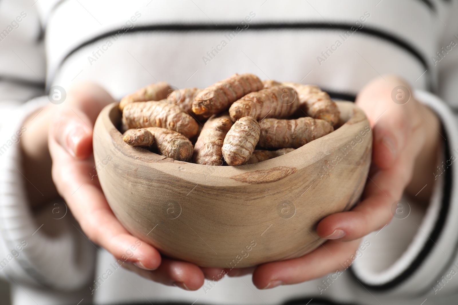 Photo of Woman holding bowl with raw turmeric roots, closeup