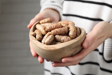 Photo of Woman holding bowl with raw turmeric roots on blurred background, closeup