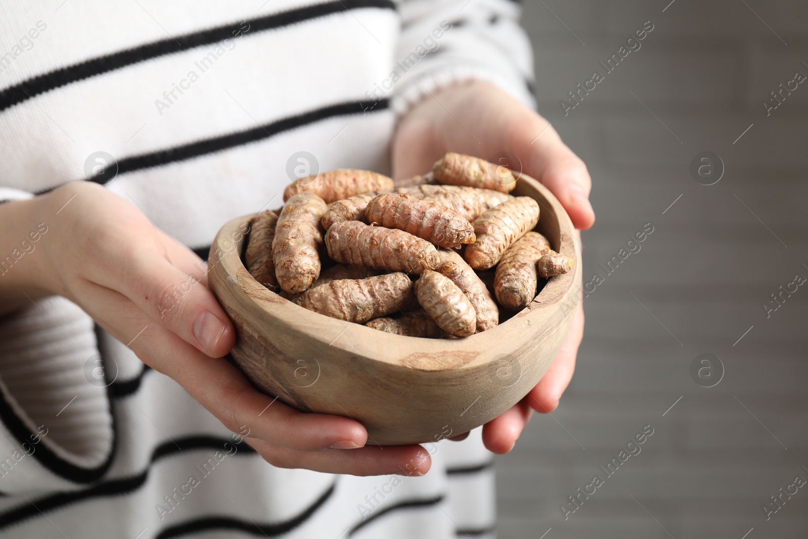 Photo of Woman holding bowl with raw turmeric roots on blurred background, closeup