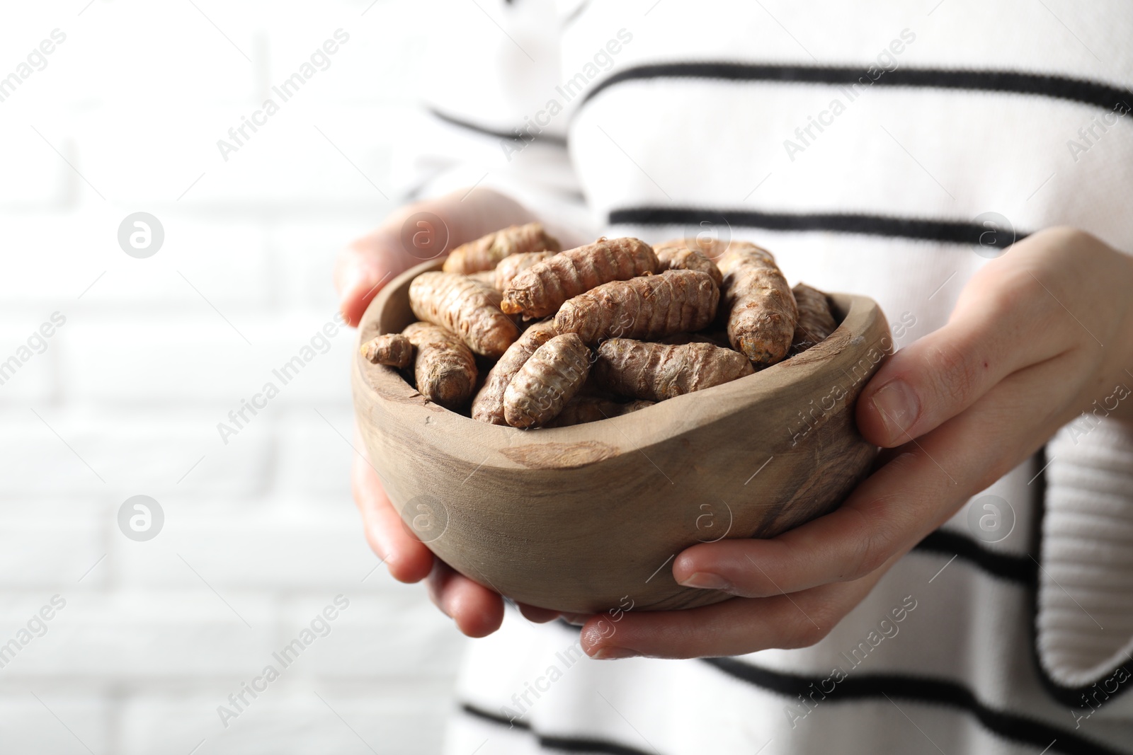 Photo of Woman holding bowl with raw turmeric roots on light background, closeup. Space for text