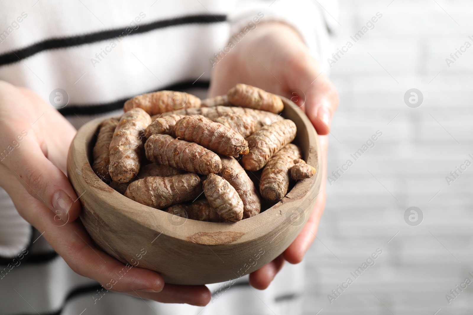 Photo of Woman holding bowl with raw turmeric roots on light background, closeup. Space for text