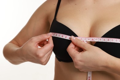 Photo of Woman in beautiful bra measuring breast circumference on white background, closeup