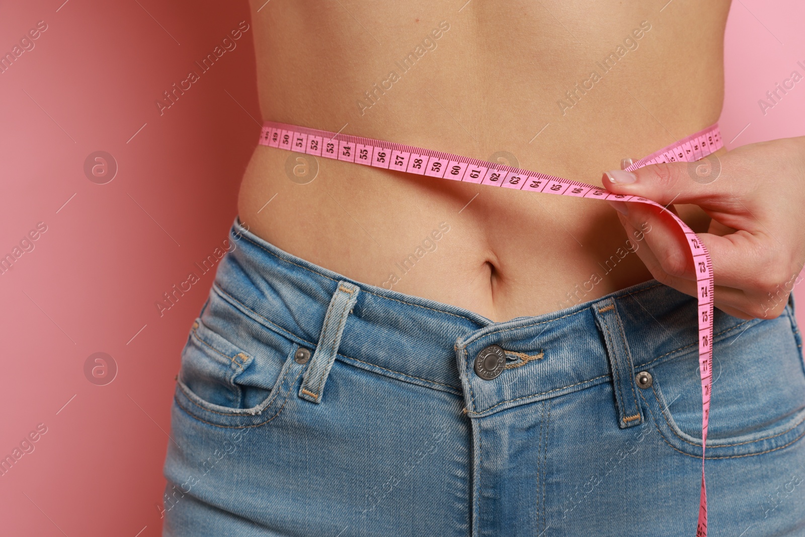 Photo of Woman measuring waist circumference on pink background, closeup