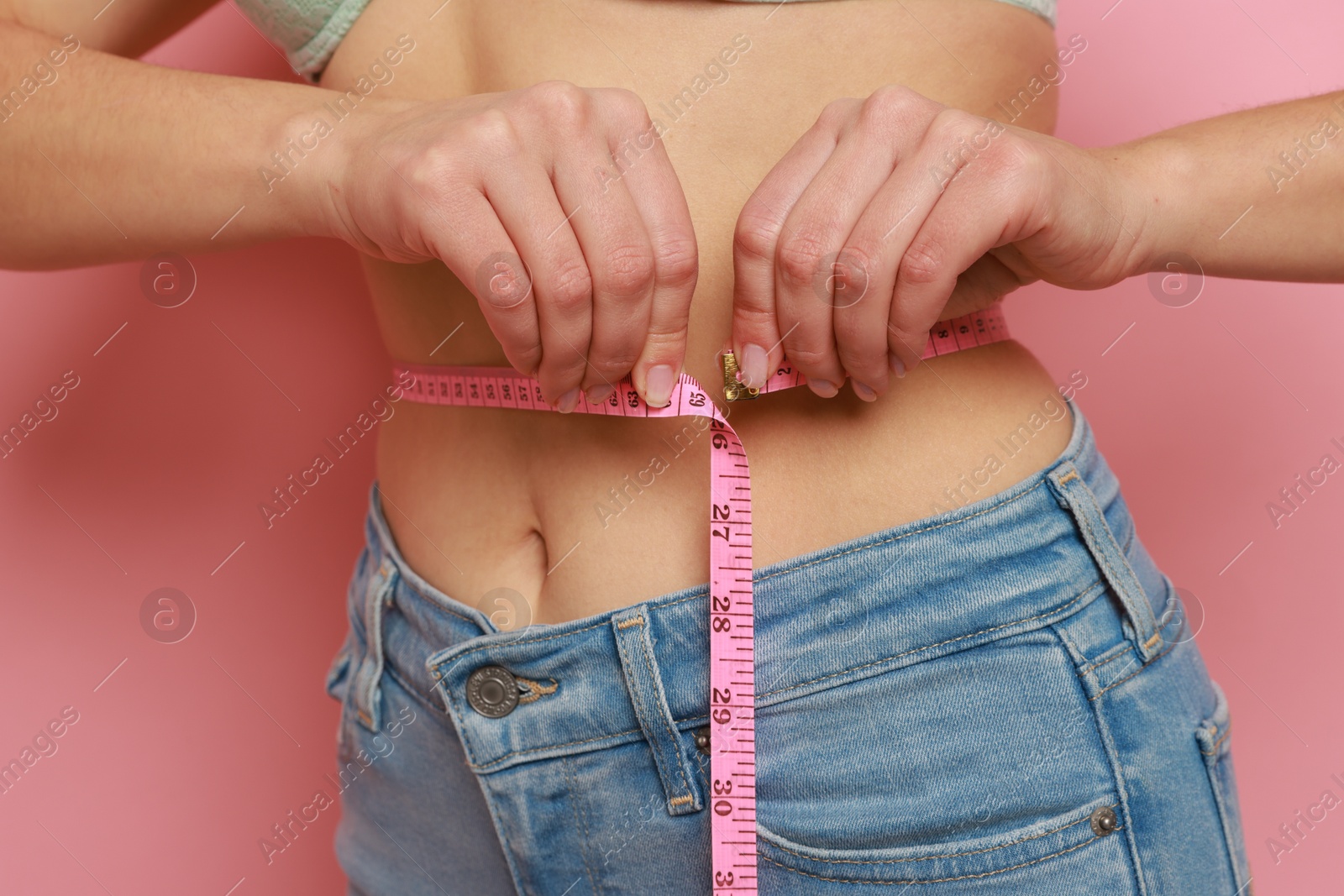 Photo of Woman measuring waist circumference on pink background, closeup