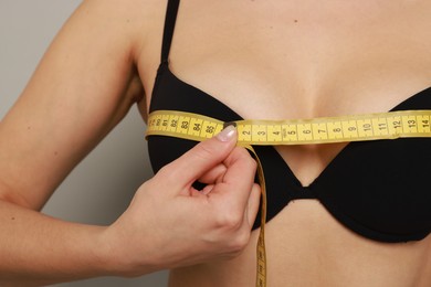 Photo of Woman in beautiful bra measuring breast circumference on light background, closeup