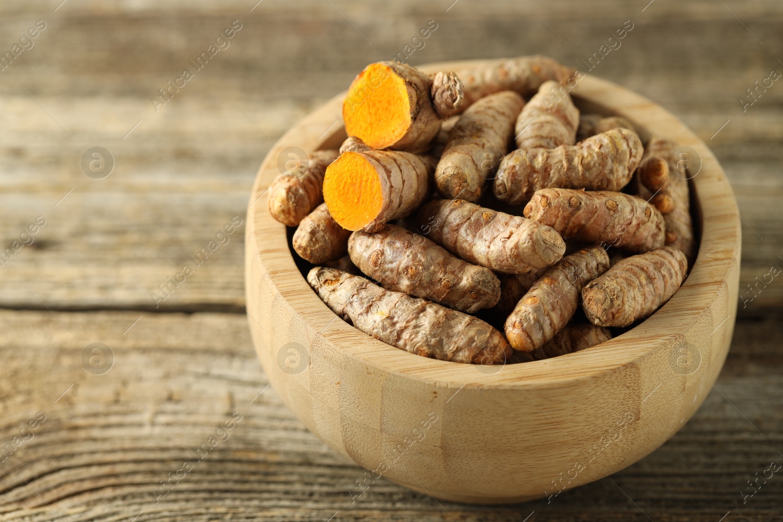 Photo of Tumeric rhizomes in bowl on wooden table, closeup