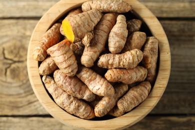 Photo of Tumeric rhizomes in bowl on wooden table, top view