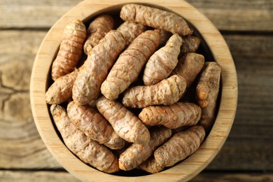 Photo of Tumeric rhizomes in bowl on wooden table, top view