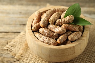 Photo of Tumeric rhizomes with leaves in bowl on wooden table, closeup