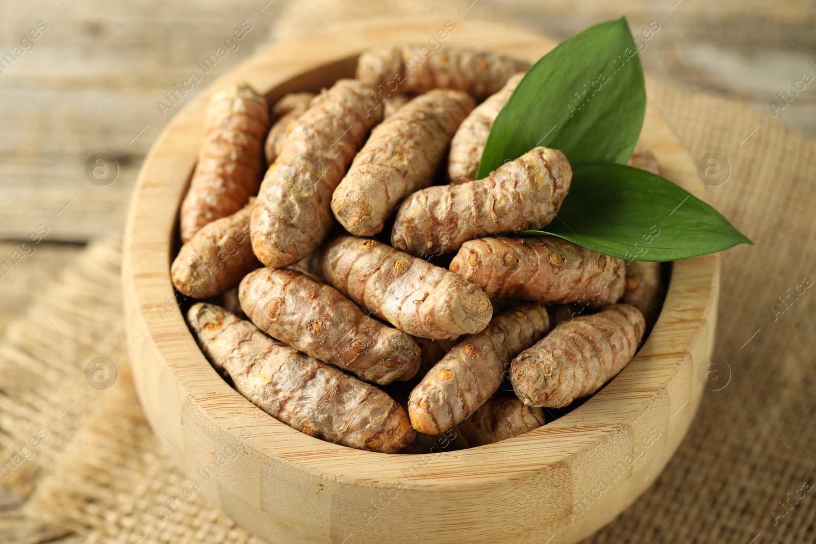 Photo of Tumeric rhizomes with leaves in bowl on table, closeup