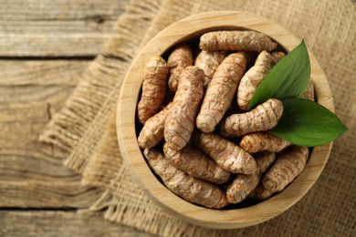 Photo of Tumeric rhizomes with leaves in bowl on wooden table, top view