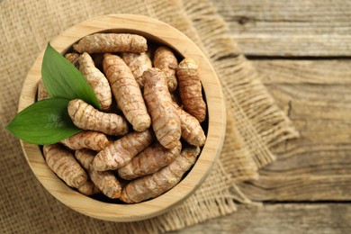 Photo of Tumeric rhizomes with leaves in bowl on wooden table, top view