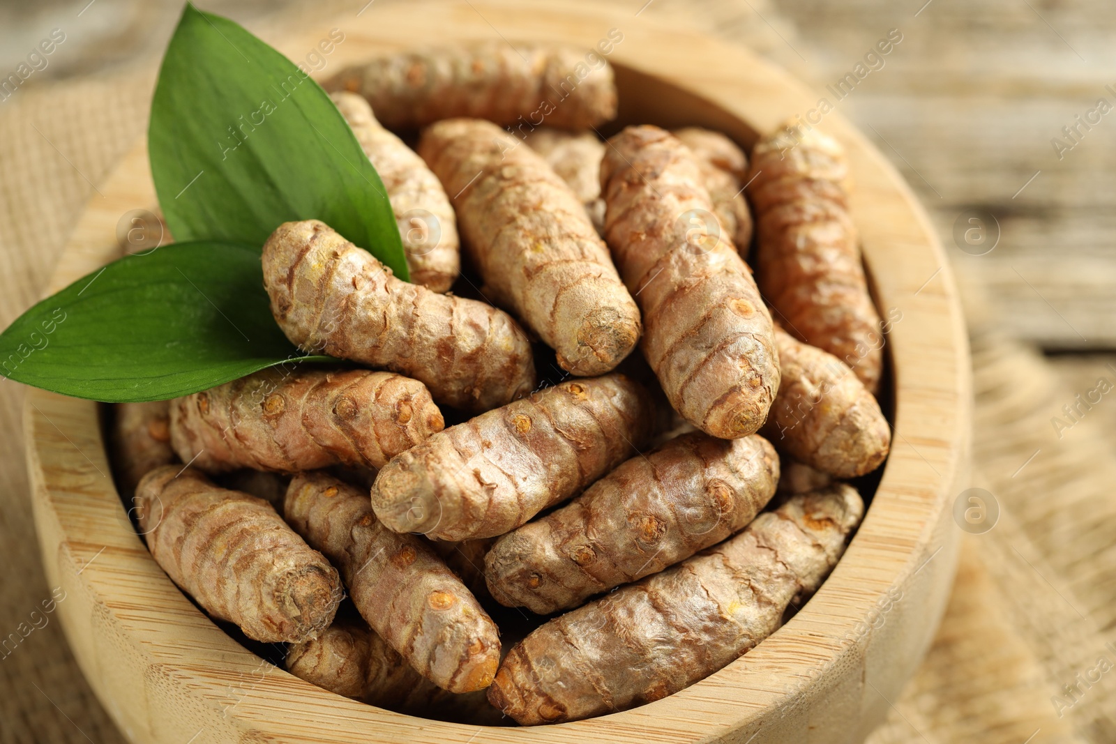 Photo of Tumeric rhizomes with leaves in bowl on table, closeup