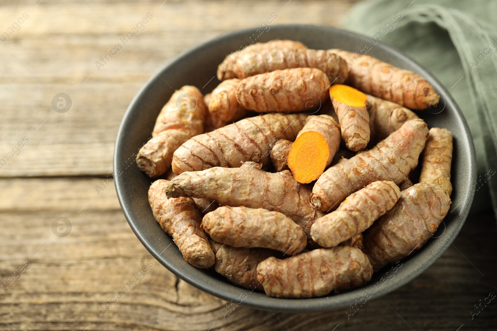 Photo of Tumeric rhizomes in bowl on wooden table, closeup