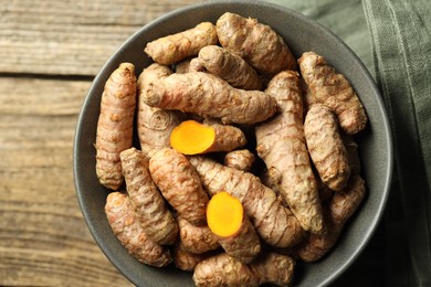 Photo of Tumeric rhizomes in bowl on wooden table, top view