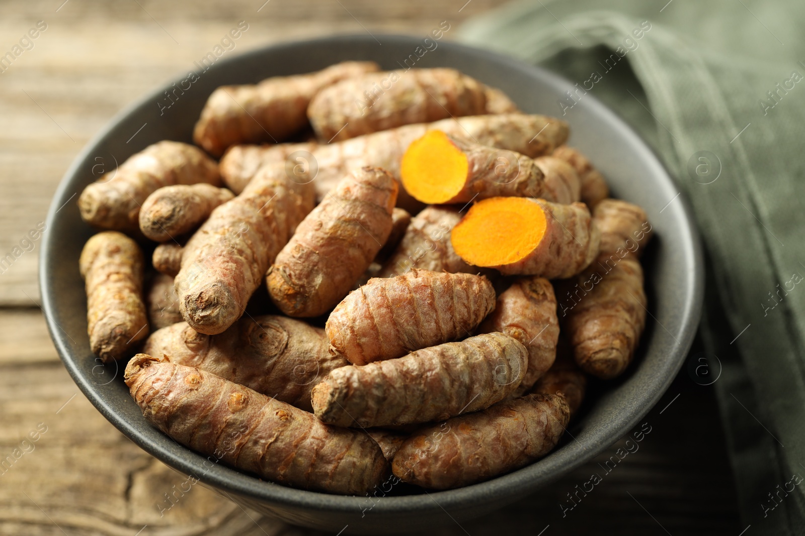 Photo of Tumeric rhizomes in bowl on wooden table, closeup