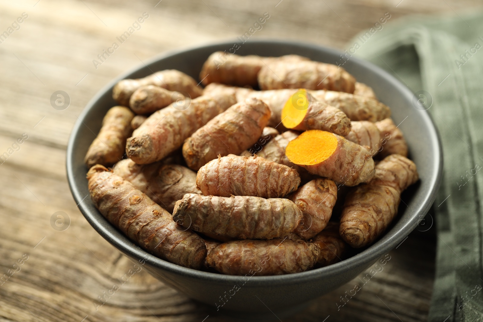 Photo of Tumeric rhizomes in bowl on wooden table, closeup