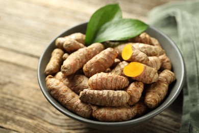 Photo of Tumeric rhizomes with leaves in bowl on wooden table, closeup