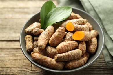 Photo of Tumeric rhizomes with leaves in bowl on wooden table, closeup