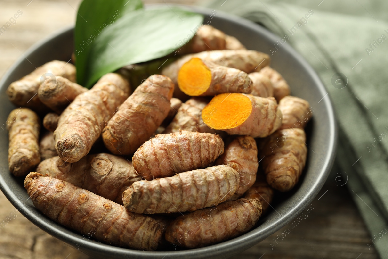 Photo of Tumeric rhizomes with leaves in bowl on table, closeup