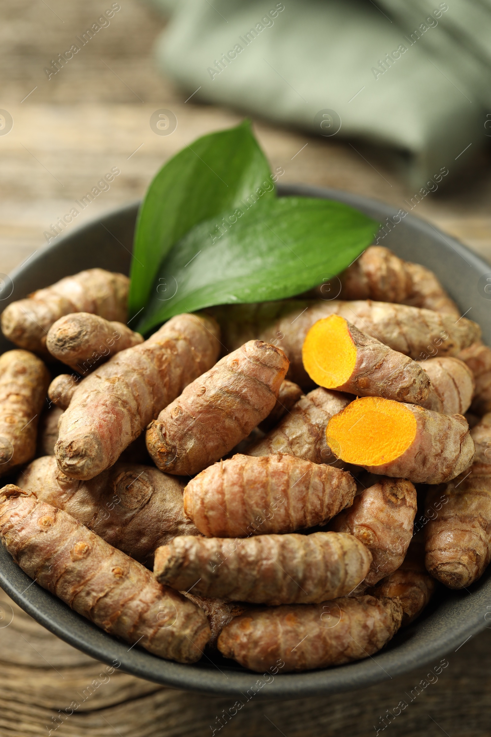 Photo of Tumeric rhizomes with leaves in bowl on wooden table, closeup