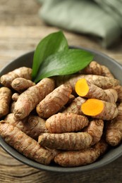 Photo of Tumeric rhizomes with leaves in bowl on wooden table, closeup