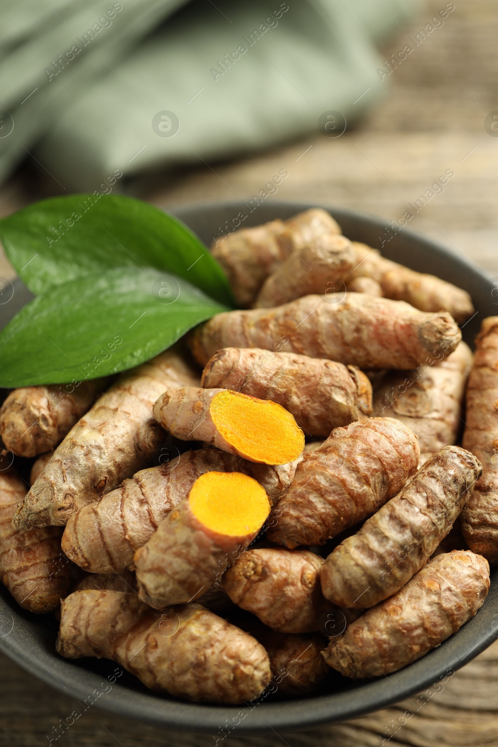 Photo of Tumeric rhizomes with leaves in bowl on wooden table, closeup