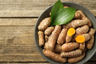 Photo of Tumeric rhizomes with leaves in bowl on wooden table, top view. Space for text