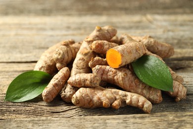 Photo of Pile of tumeric rhizomes with leaves on wooden table, closeup