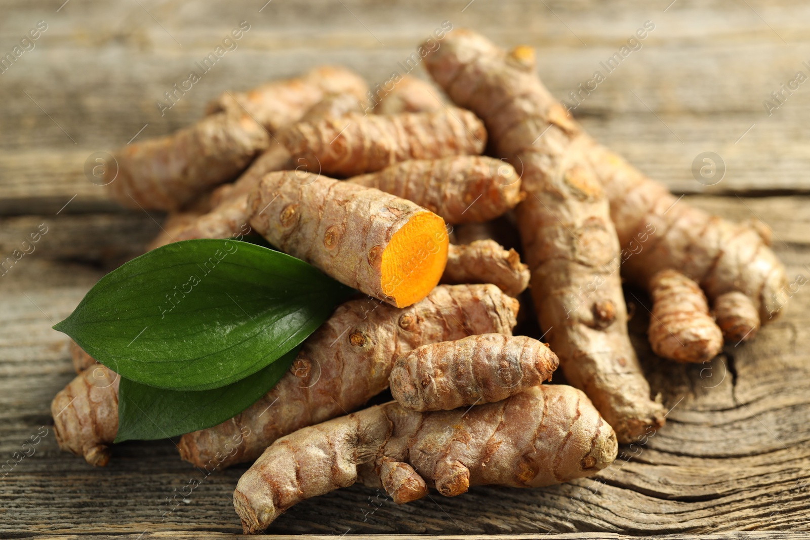 Photo of Pile of tumeric rhizomes with leaves on wooden table, closeup