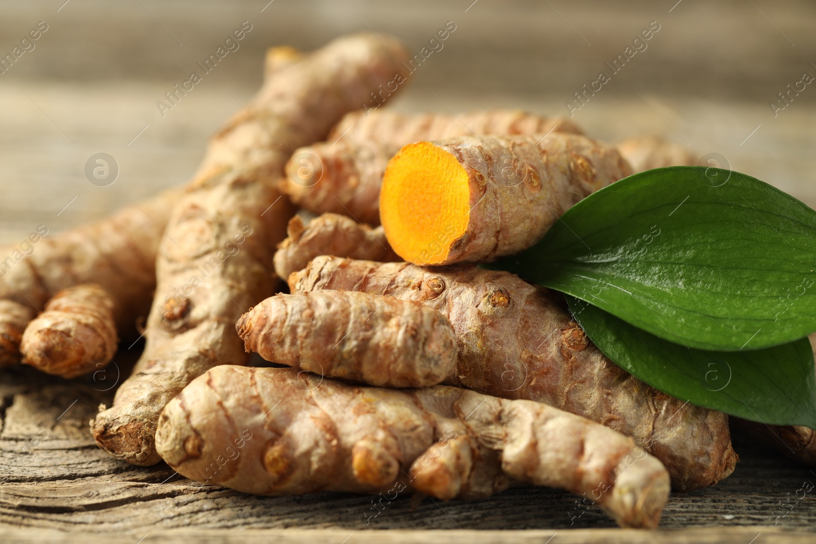 Photo of Pile of tumeric rhizomes with leaves on wooden table, closeup