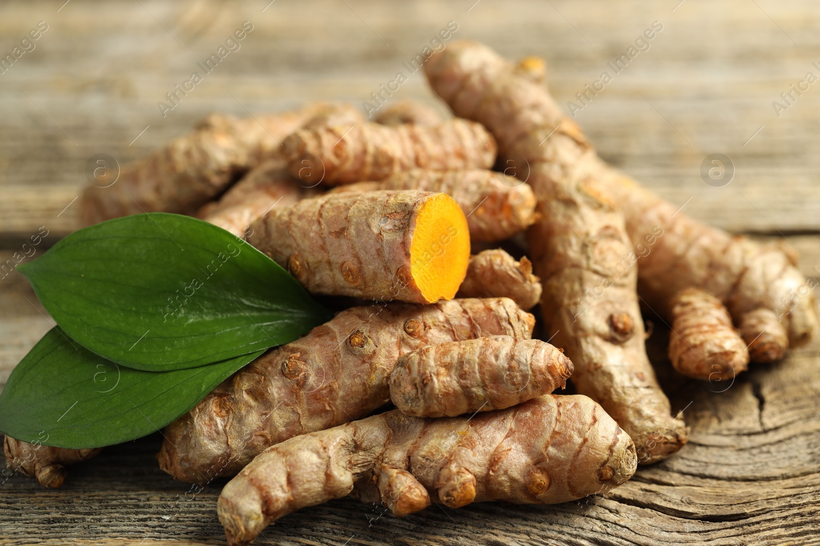 Photo of Pile of tumeric rhizomes with leaves on wooden table, closeup