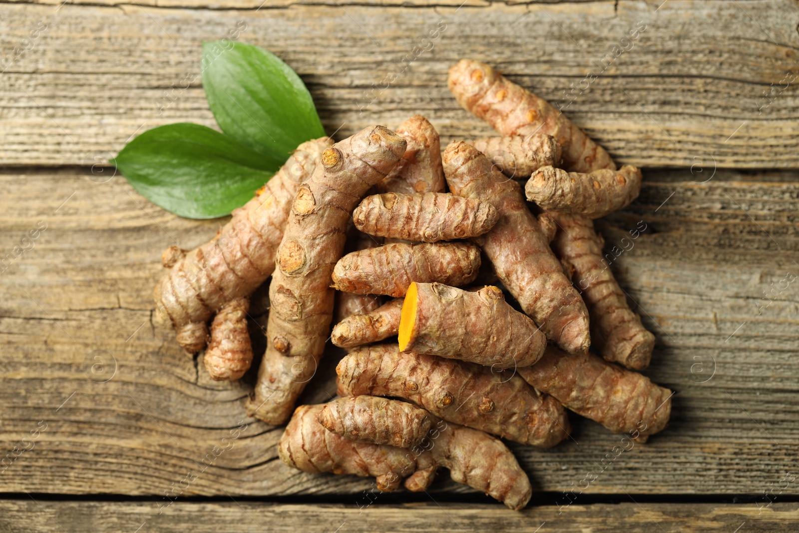 Photo of Pile of tumeric rhizomes with leaves on wooden table, top view