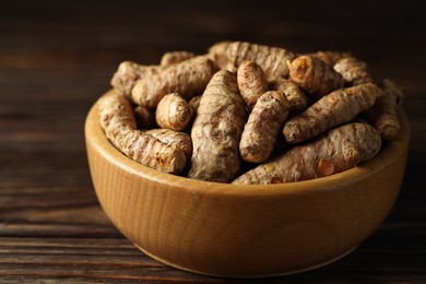 Photo of Tumeric rhizomes in bowl on wooden table, closeup