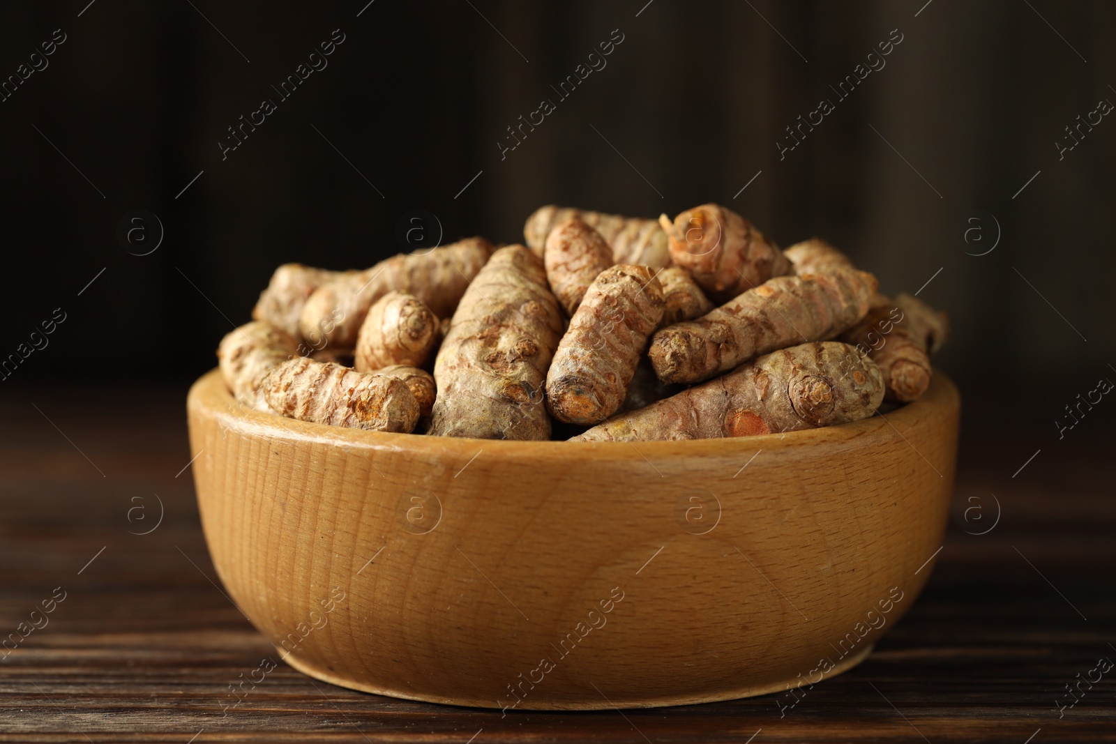 Photo of Tumeric rhizomes in bowl on wooden table, closeup