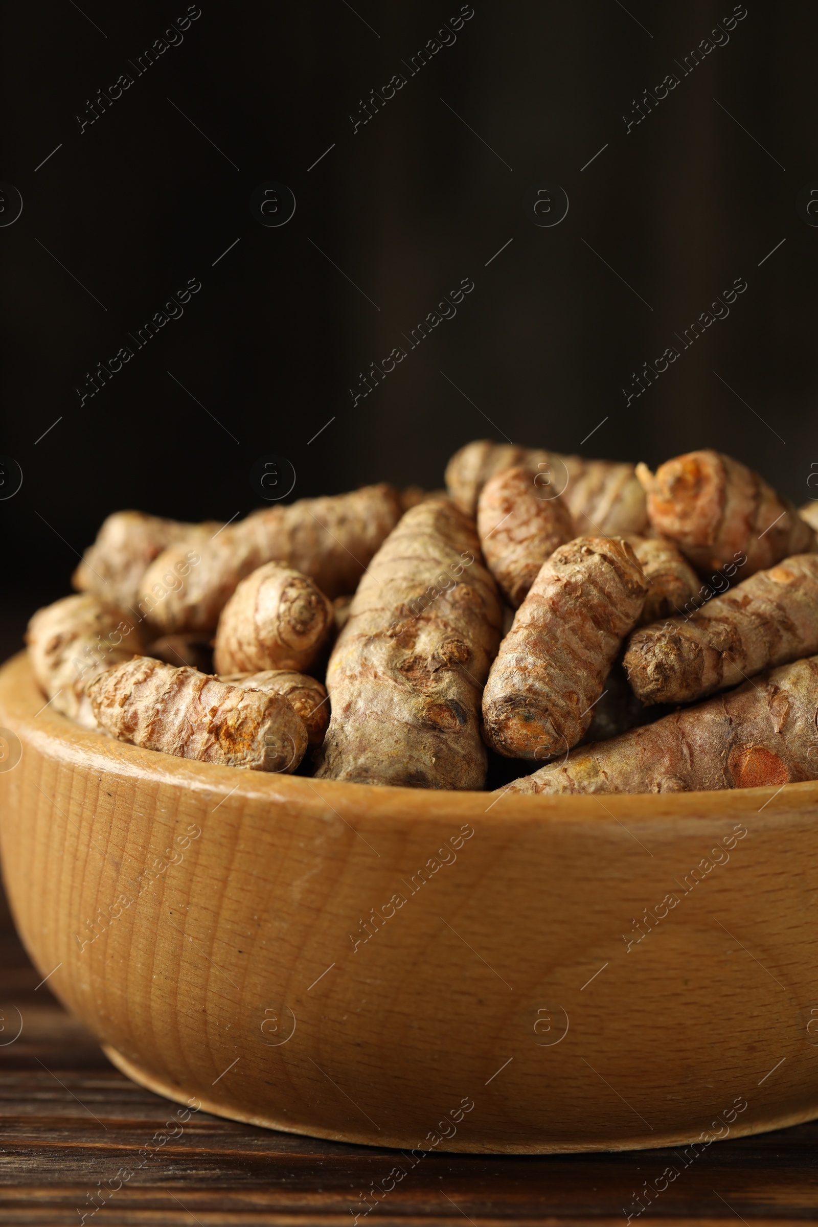 Photo of Tumeric rhizomes in bowl on wooden table, closeup