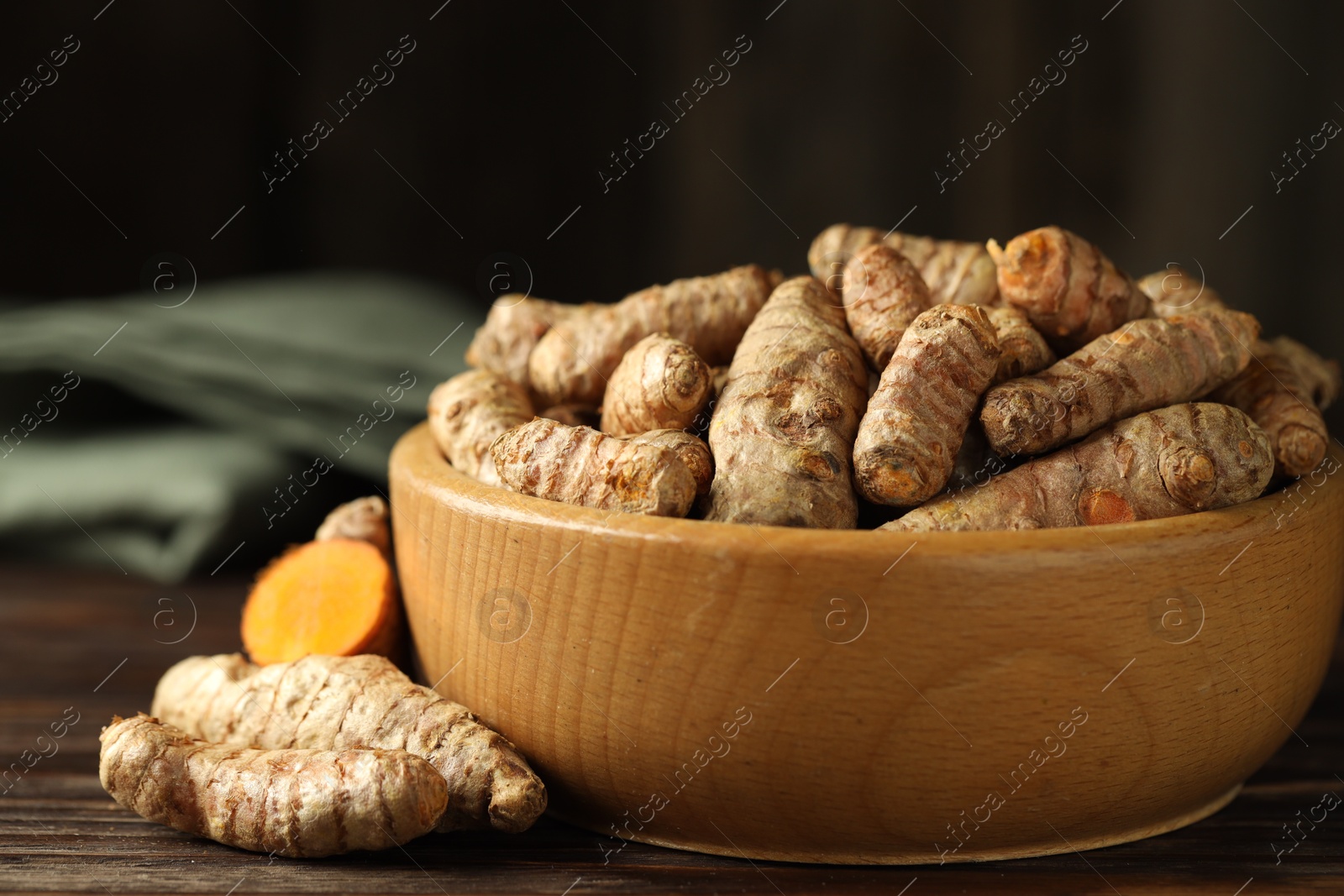 Photo of Tumeric rhizomes in bowl on wooden table, closeup