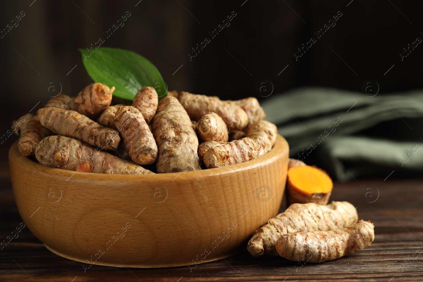 Photo of Tumeric rhizomes with leaf in bowl on wooden table, closeup