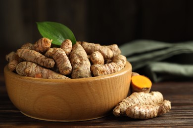 Photo of Tumeric rhizomes with leaf in bowl on wooden table, closeup