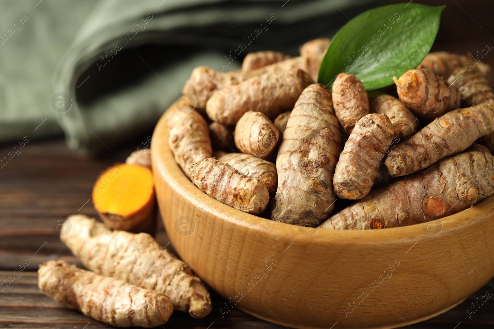 Photo of Tumeric rhizomes with leaf in bowl on wooden table, closeup