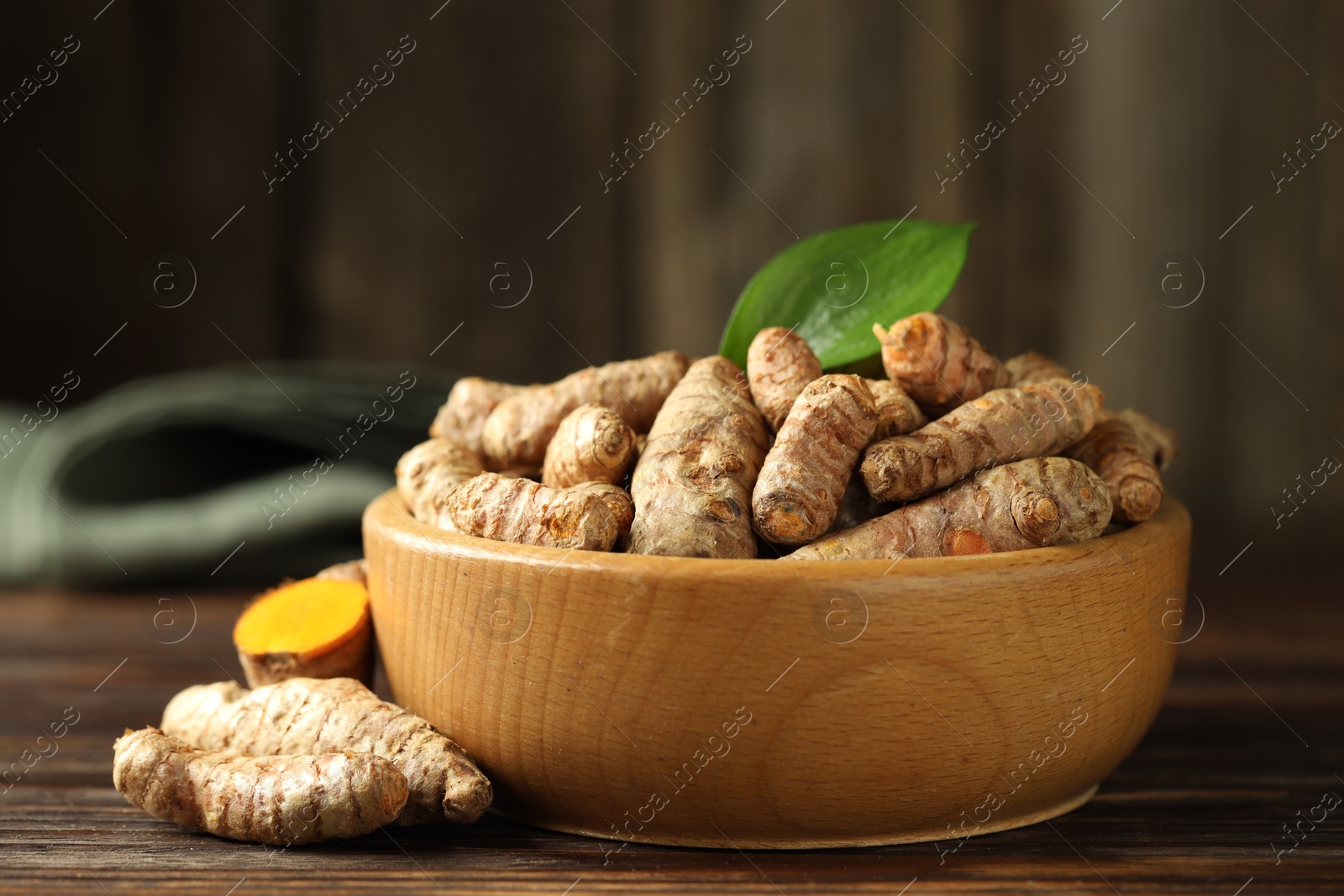 Photo of Tumeric rhizomes with leaf in bowl on wooden table, closeup