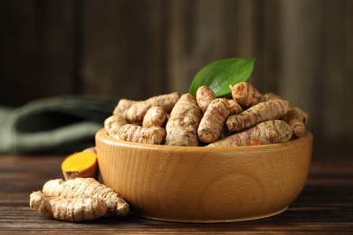 Photo of Tumeric rhizomes with leaf in bowl on wooden table, closeup