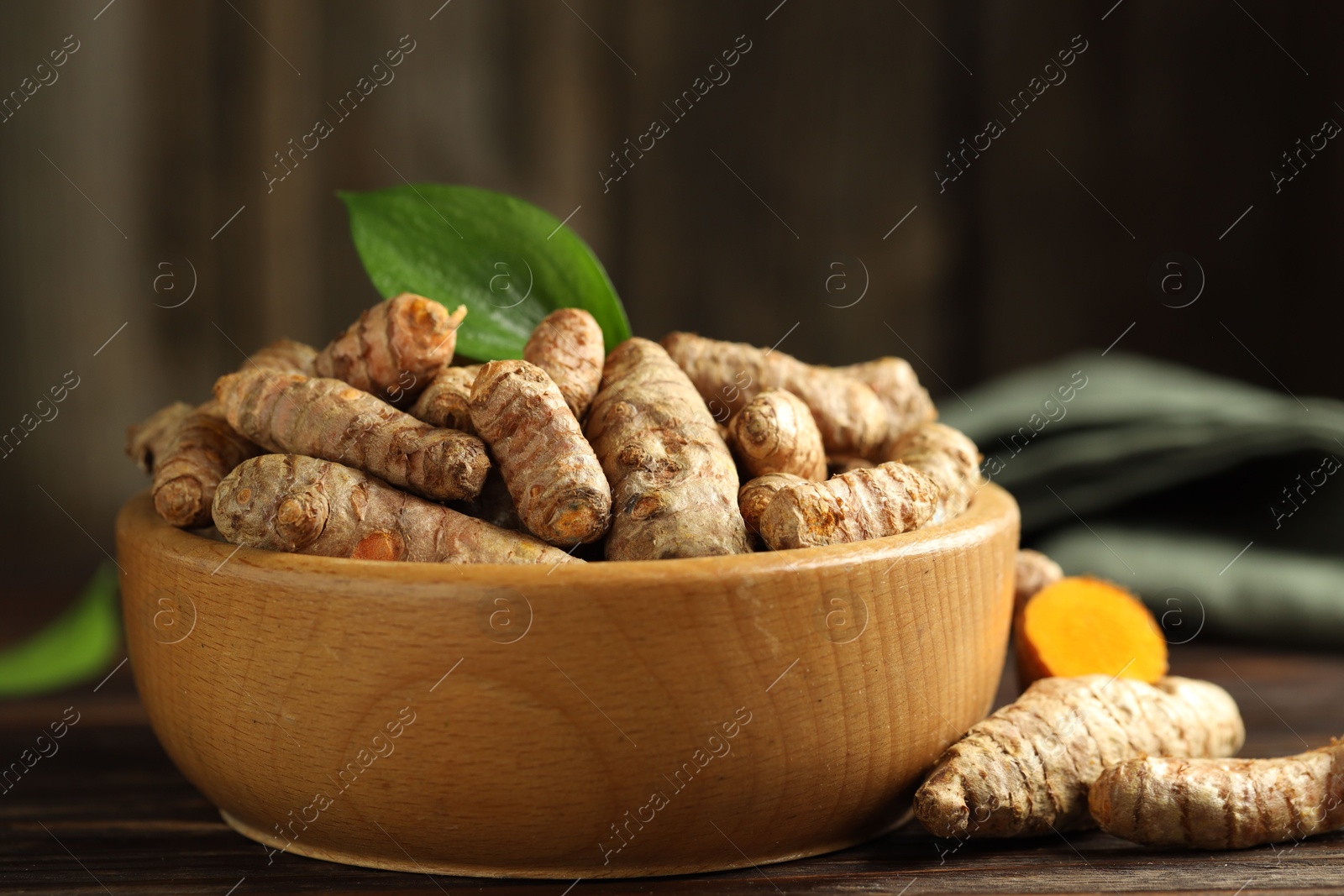 Photo of Tumeric rhizomes with leaf in bowl on wooden table, closeup