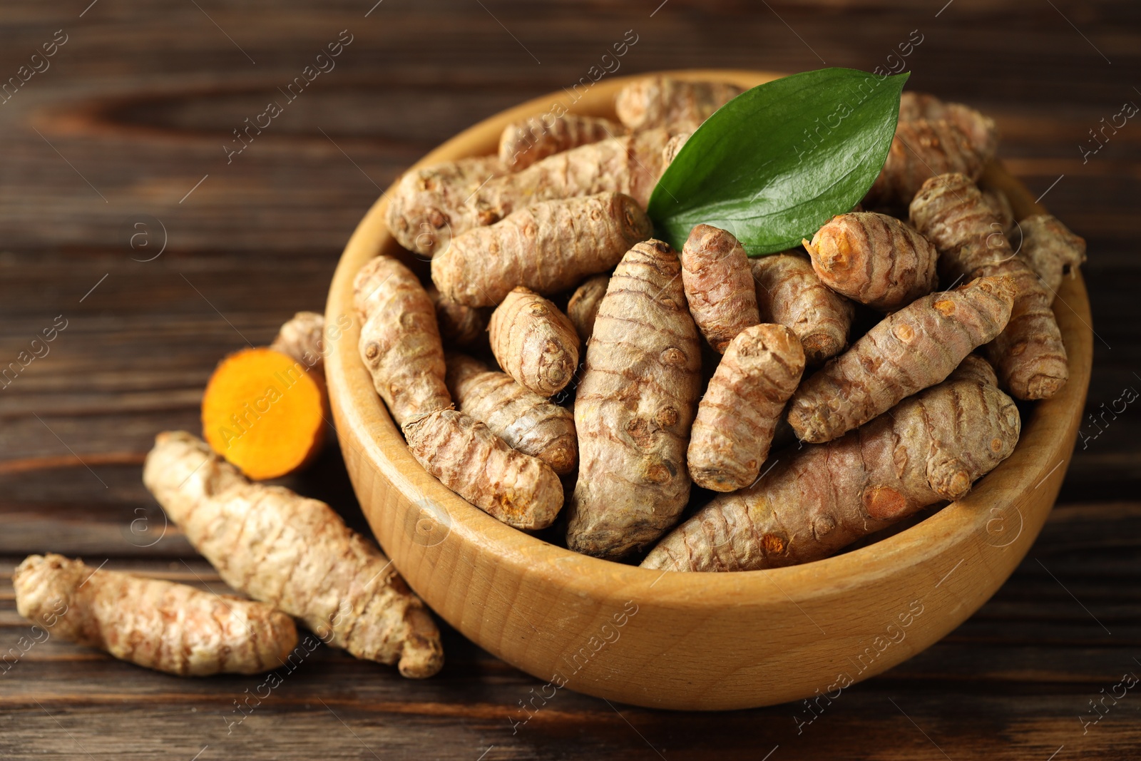 Photo of Tumeric rhizomes with leaf in bowl on wooden table, closeup