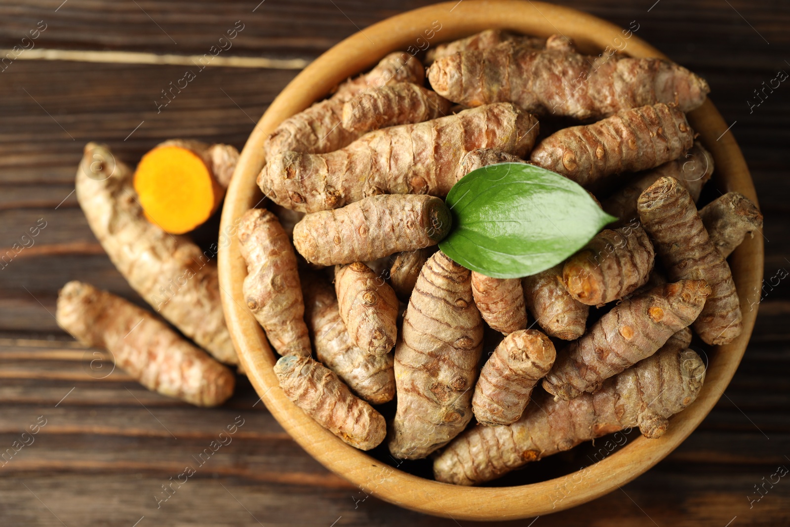 Photo of Tumeric rhizomes with leaf in bowl on wooden table, top view