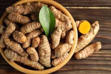 Photo of Tumeric rhizomes with leaf in bowl on wooden table, top view